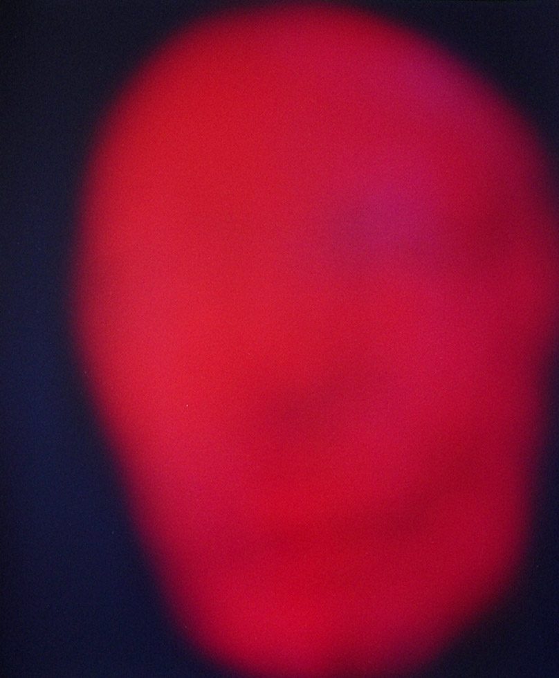 A red mask blurred against a dark background