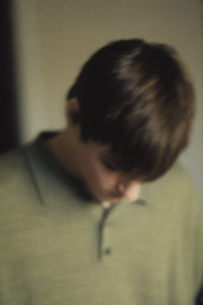 A soft focus photograph of a young man wearing a green shirt, looking down