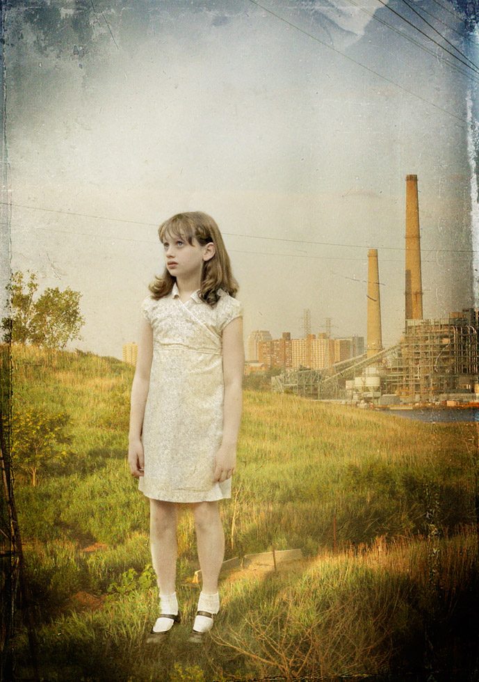 A photograph of a young girl with a look of concern looking slightly up, in the distance is a factory with two smokestacks