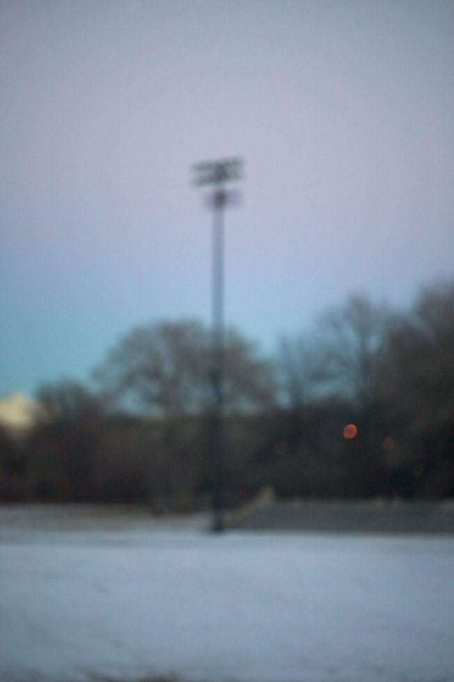 A soft focus photograph of a stadium lights post with the glow of the sun rise in the sky behind