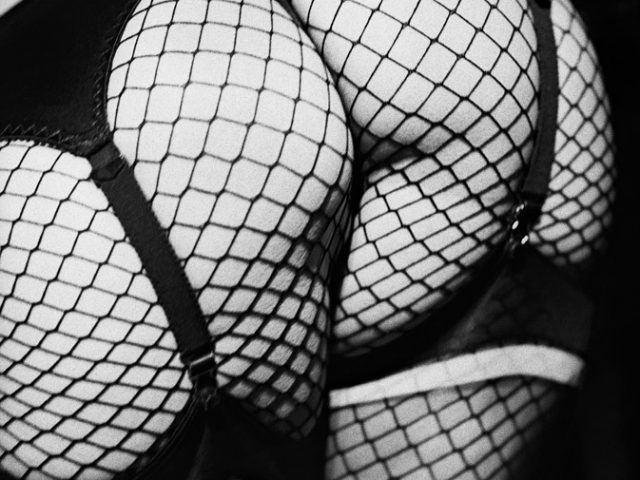 This is a black-and-white photograph of a female's backside in a garter and fishnet stockings.