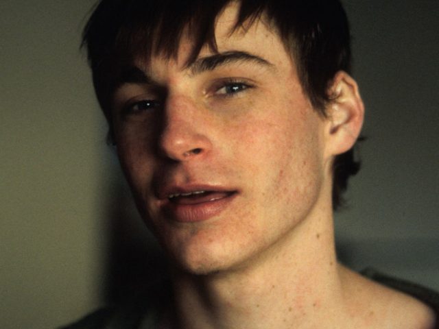 A photograph of the face of a a young man with brown hair, his mouth is slightly open