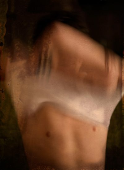 A photograph of someone removing their shirt, their face obscured by their arms