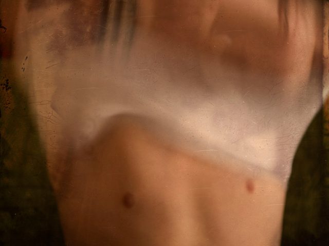 A photograph of someone removing their shirt, their face obscured by their arms