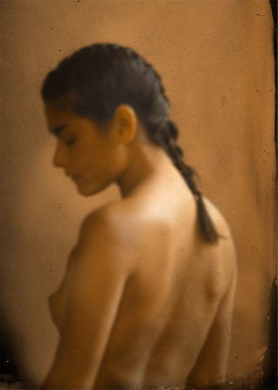 A soft focus portrait of a young woman with her back turned to the camera, her dark hair in a braid