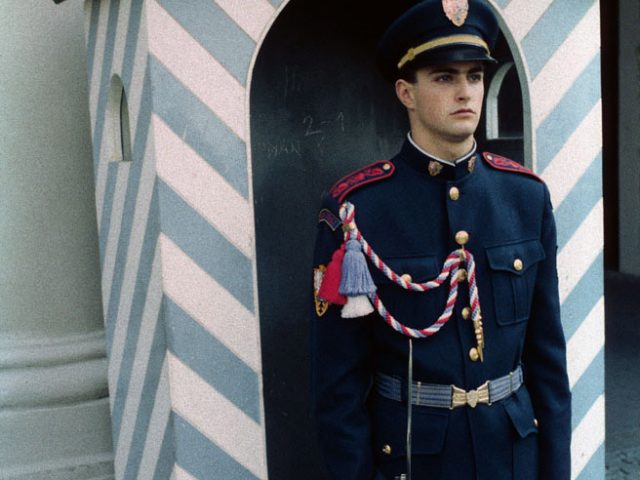 A photograph of a young soldier in uniform standing in front of a stripped sentry box