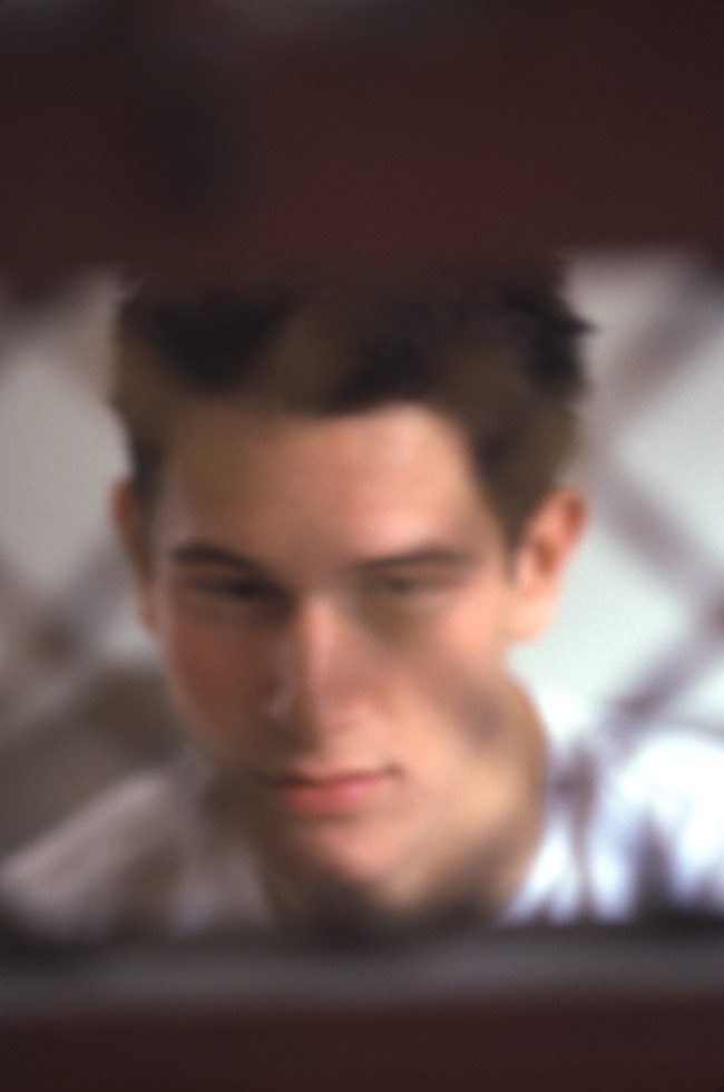 A soft focus portrait of a person seen behind what seems to be metal fencing