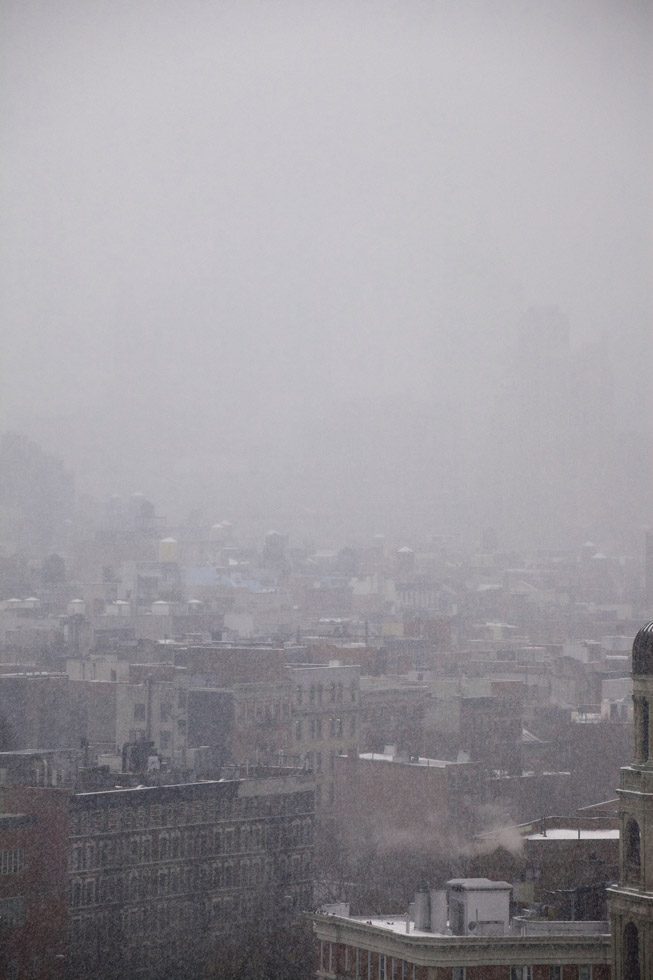 A hazy photograph of the roofs of new york as its snowing