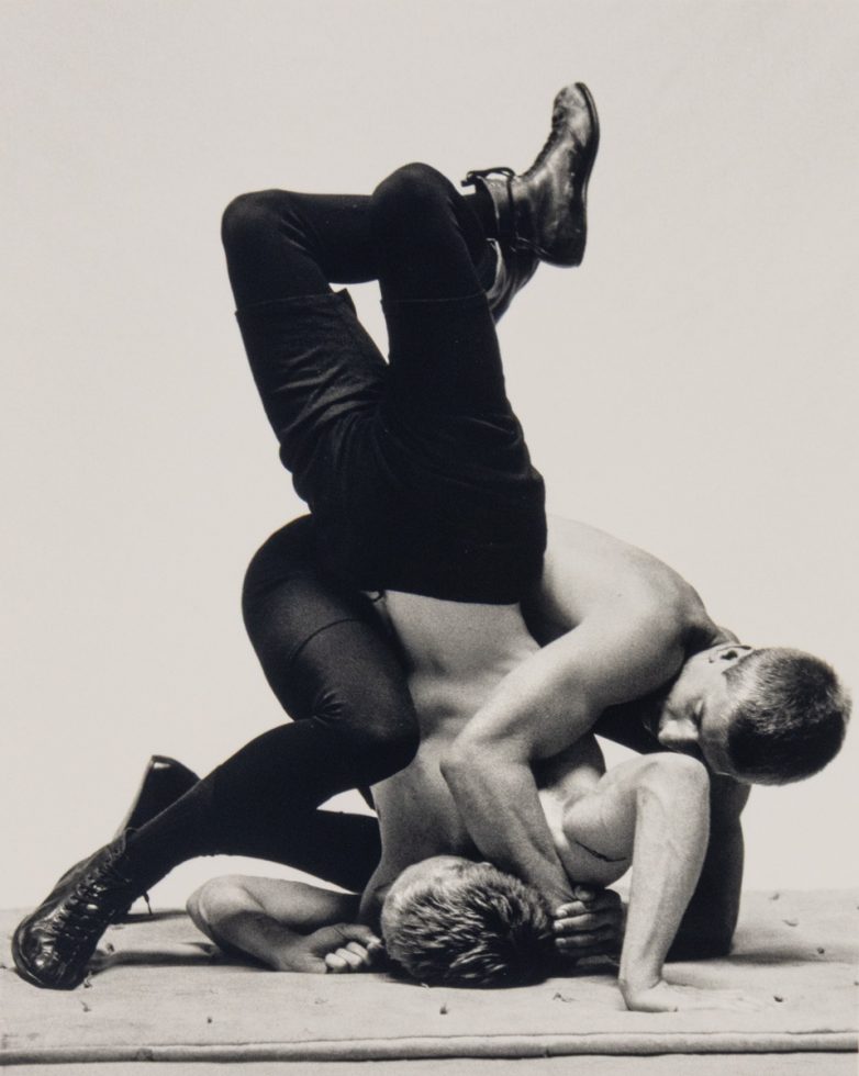This photograph shows two men wrestling with one another. One pins the other against the ground.