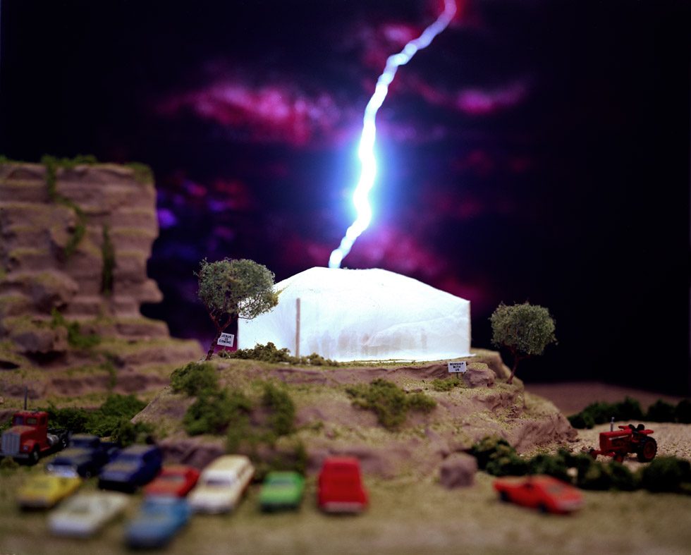 This is a color photograph of a lightning bolt striking a tent with people inside and cars parked outside.