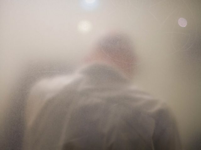 Photograph of the back of a man seen through a slightly hazy window