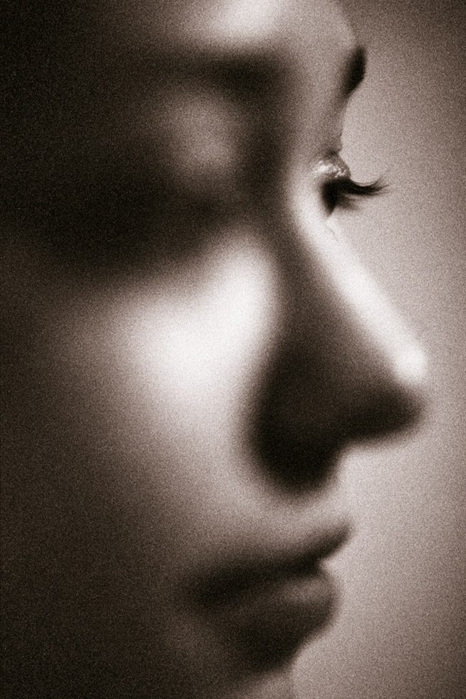 This is a sepia-toned, black-and-white close-up photograph of a woman's face in profile.