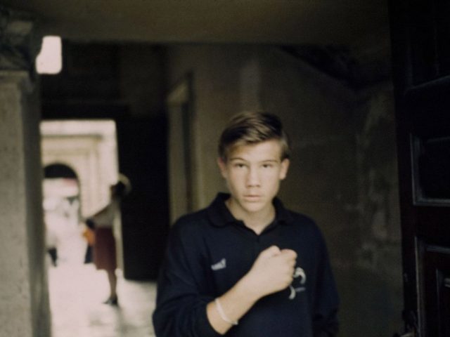 A photograph of a young boy wearing a black polo looking straight into the camera