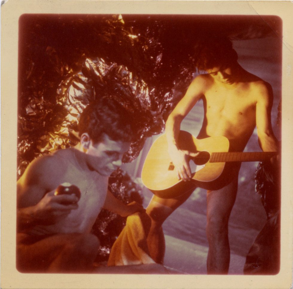 A photograph by James Bidgood of two boys in a cave. One is playing the guitar.