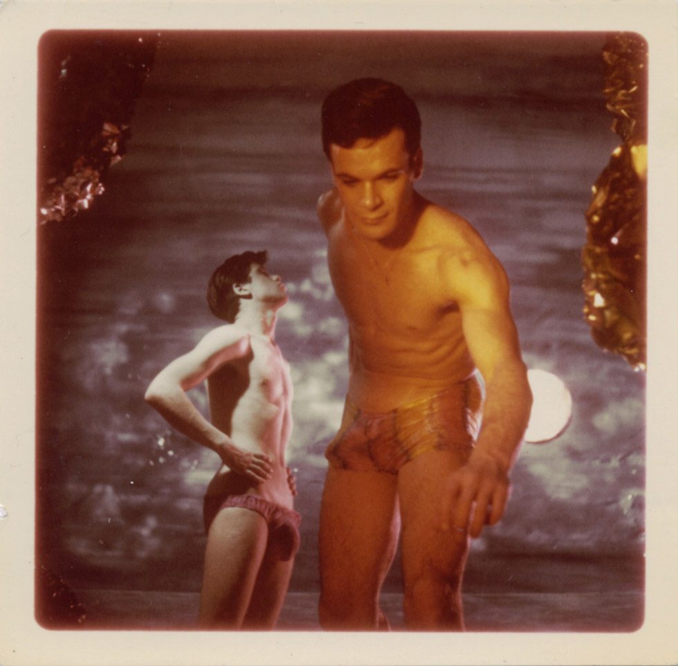 A staged photograph by James Bidgood of two men in a moonlit cave, one reaching towards the viewer, the other looking up at the sky