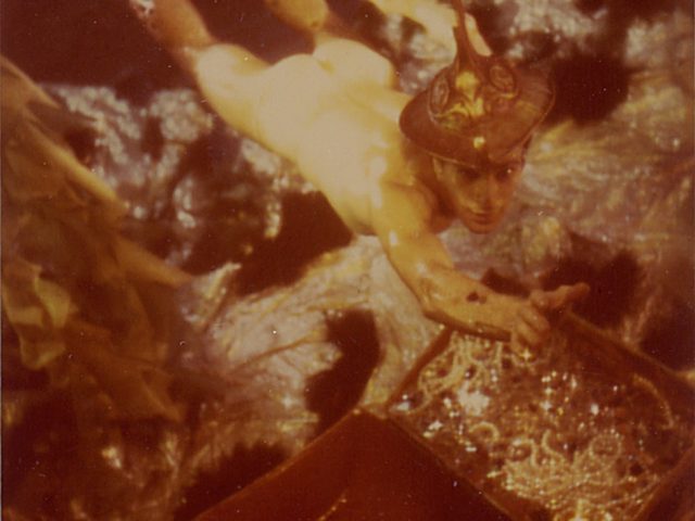 James Bidgood photograph from the 1960s of a nude man swimming underwater reaching out to a treasure chest