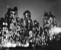 A black and white photograph of various buildings rendered with motion blur at night.