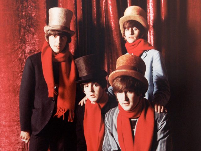 A color photograph of four men in top hats and red scarves against a shiny, red drapery.