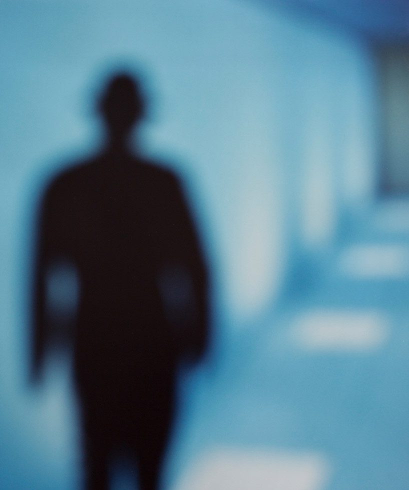 A black figure in a long blue hallway.