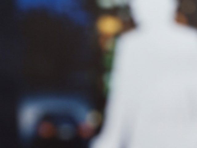 A blurry image of a man in a suit standing before a large building, creating an air of professionalism and mystery.