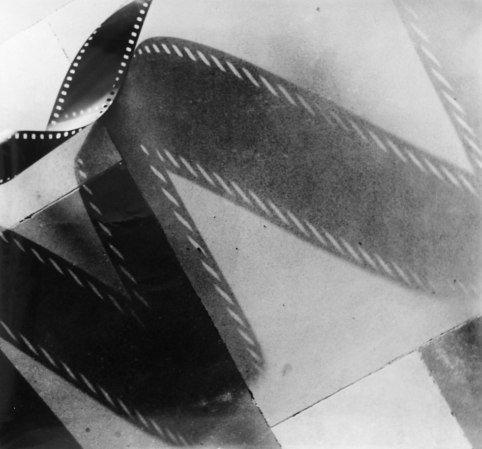 This is a black and white photograph of a strip of negative film casting a shadow.
