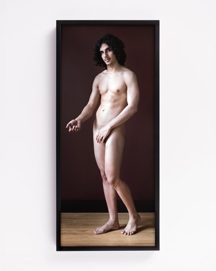 This color photograph shows a naked figure standing up with their arm outstretched.