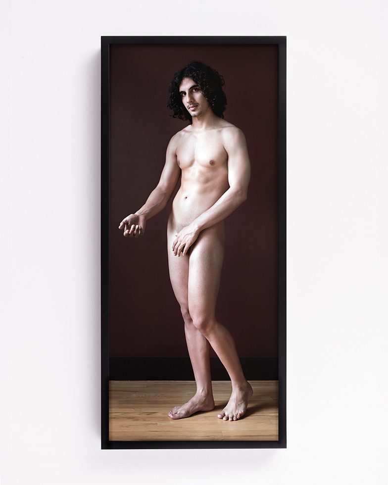 This color photograph shows a naked figure standing up with their arm outstretched.