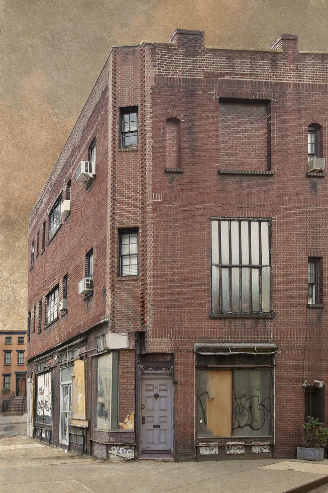 A photograph of the side of a New York City brick building with a boarded up store front on the ground floor