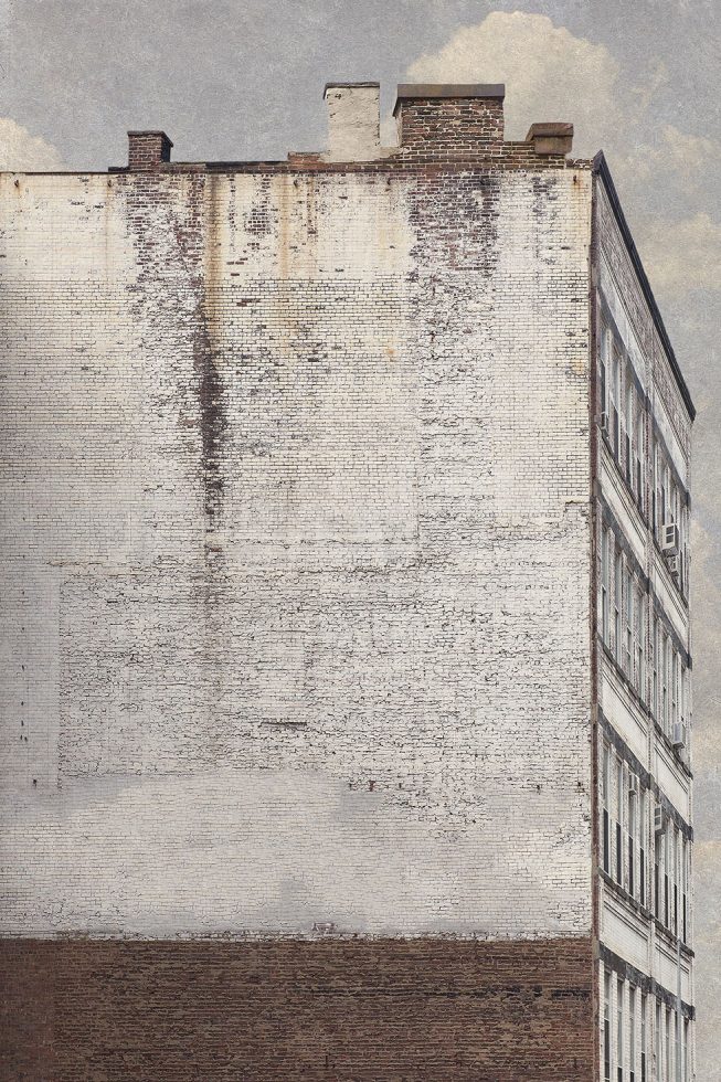 A photograph of the side of a brick building, the top half of the bricks of the building are painted white