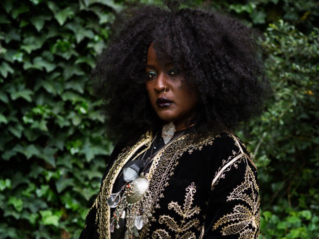 This is a color photograph of a striking Black woman in three-quarter profile wearing an embroidered robe and a lot of jewelry.