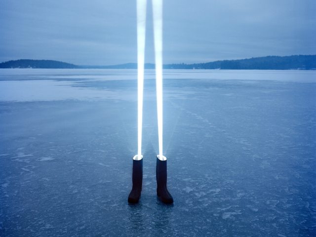 An image of a pair of rubber boots on a frozen lake with beams of light shining upward out of each.