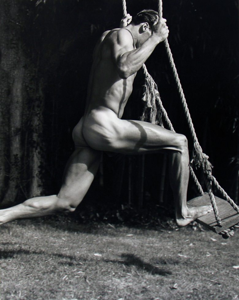 Photograph of a nude man with one foot on a wooden swing