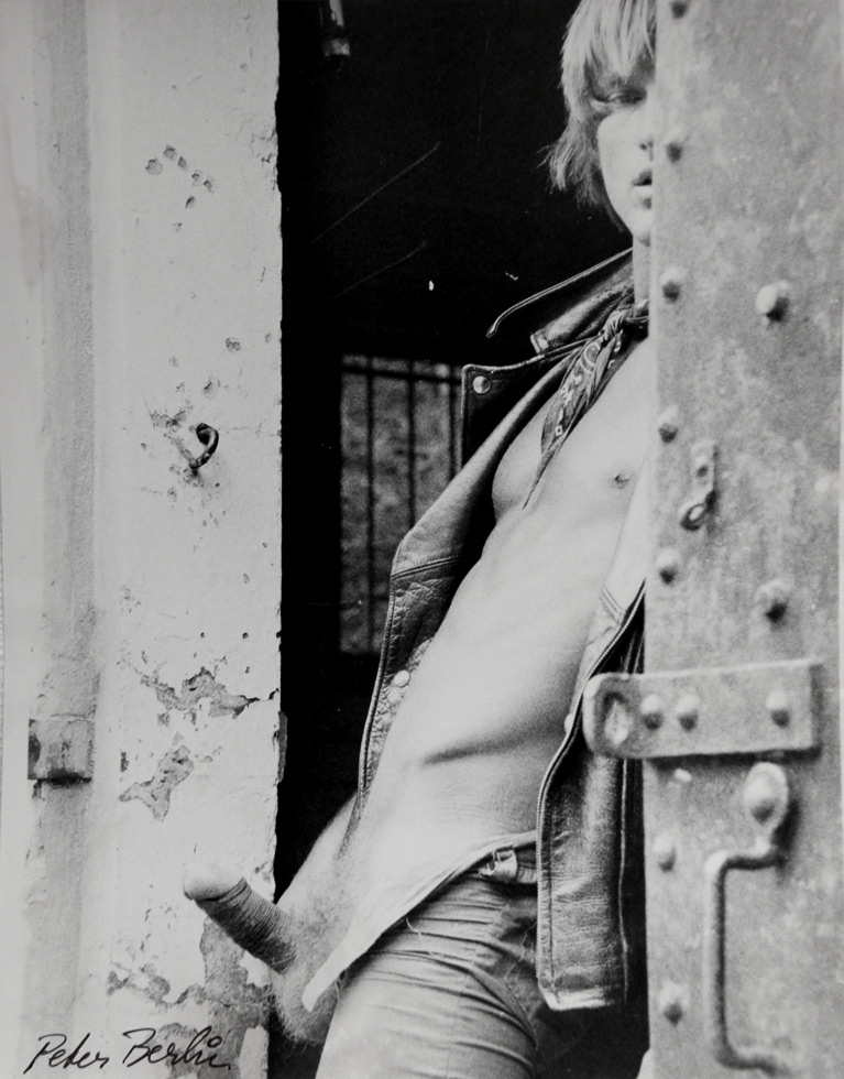 A black-and-white photograph of a man hiding behind a large steel door.