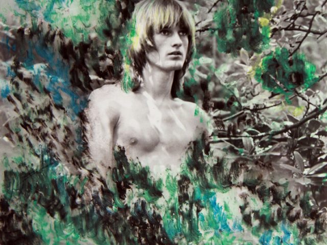 Photograph of Peter Berlin without a shirt standing amongst hand painted bushes