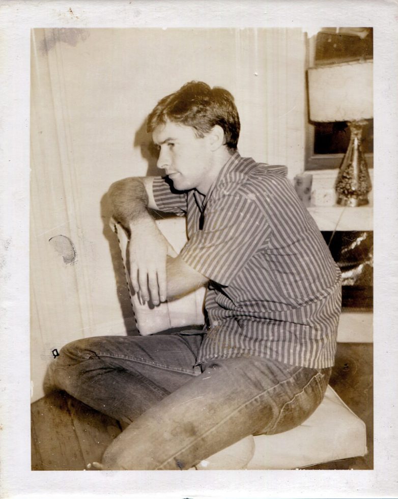 A Polaroid print of a seated man in a striped shirt and jeans seen in profile.