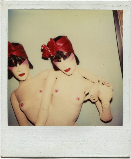 This is a color Polaroid of two twin female dolls without clothes and red headscarves.