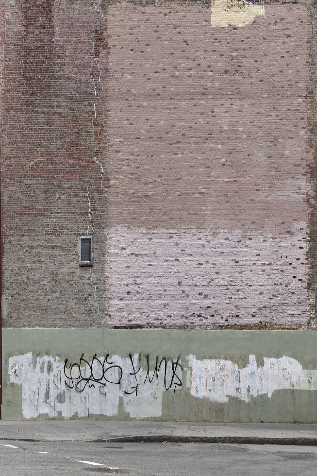 A photograph of the side of a brick building along the bottom is a wood barrier painted green