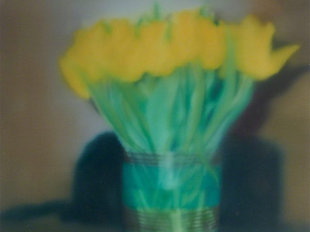 This is a blurry, soft-focus image of yellow tulips in a green striped vase.
