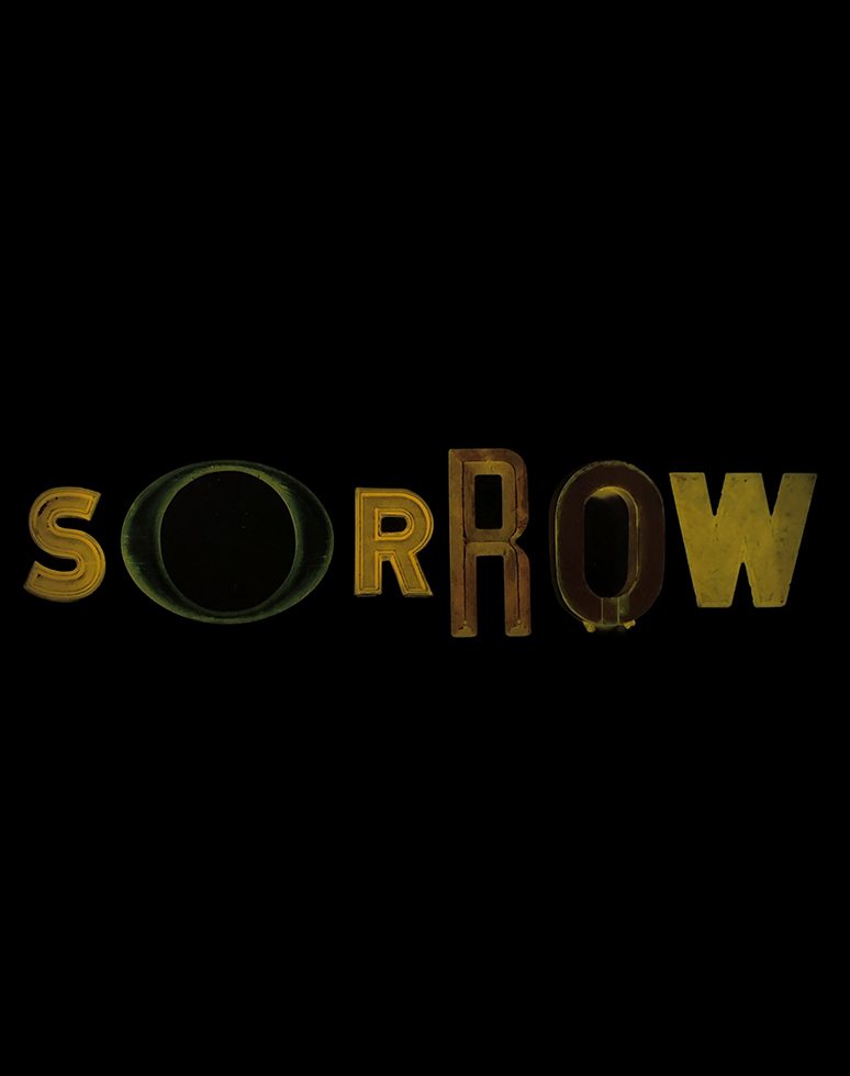 This is a color photograph of different shaped letters on a black background spelling the word "sorrow."