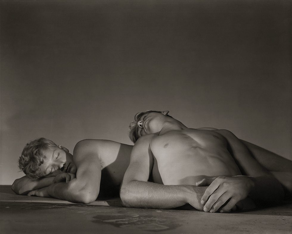 This is a black-and-white photograph of two shirtless young men posed as though they are sleeping.