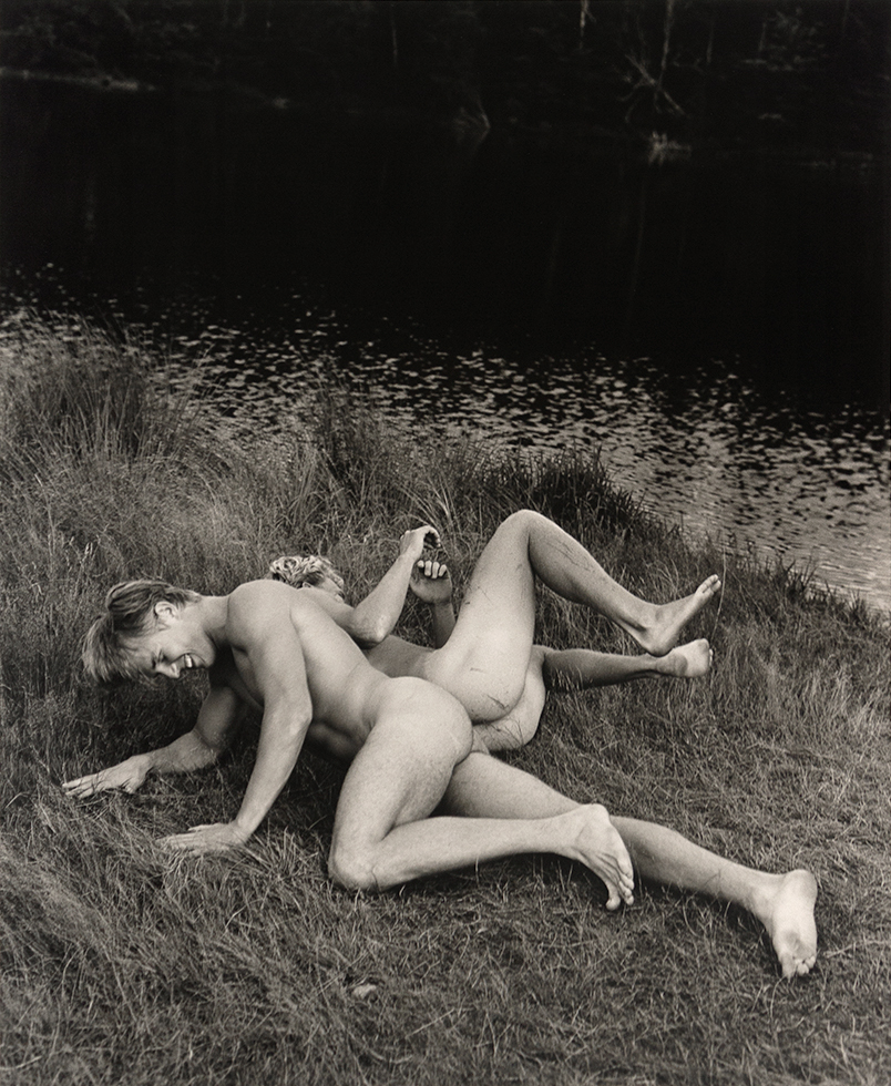 Two young men rolling in the grass on the edge of a lake