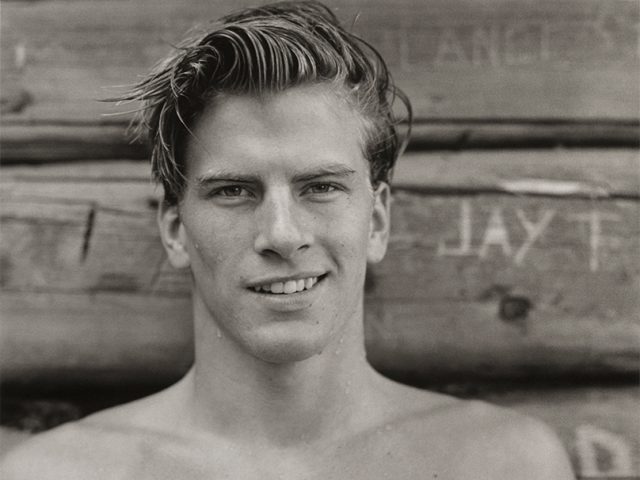 Black and white portrait of a young man smiling at the camera with water dripping off him