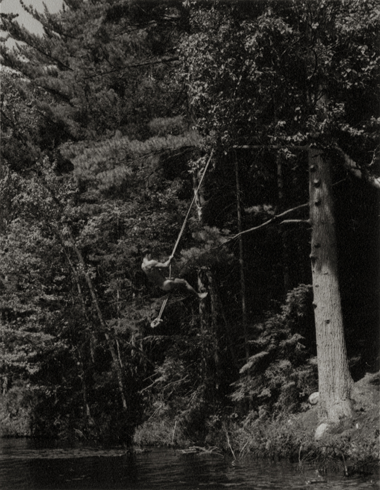 Photograph of a man swinging on a rope above a lake