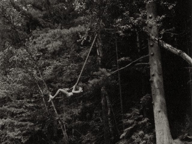 Black and white photograph of a man swinging on a rope above a lake