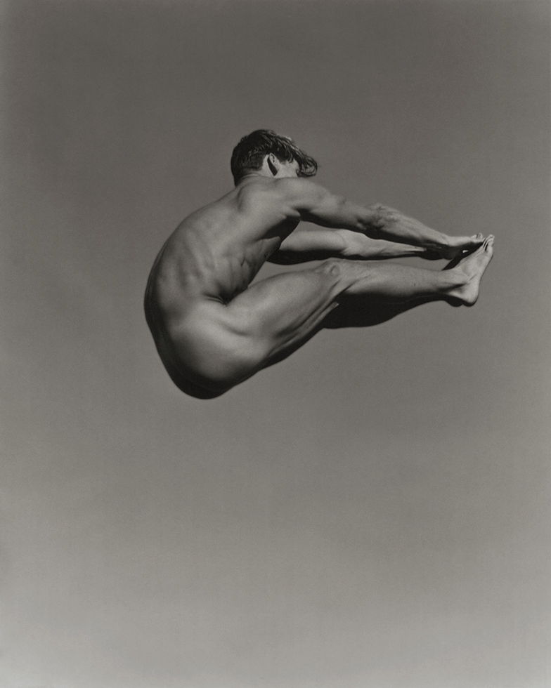 Black and white photograph of a man in the air touching his toes