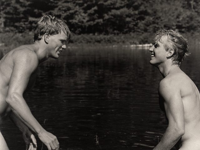 Two young blonde men facing each other and smiling white standing in a lake