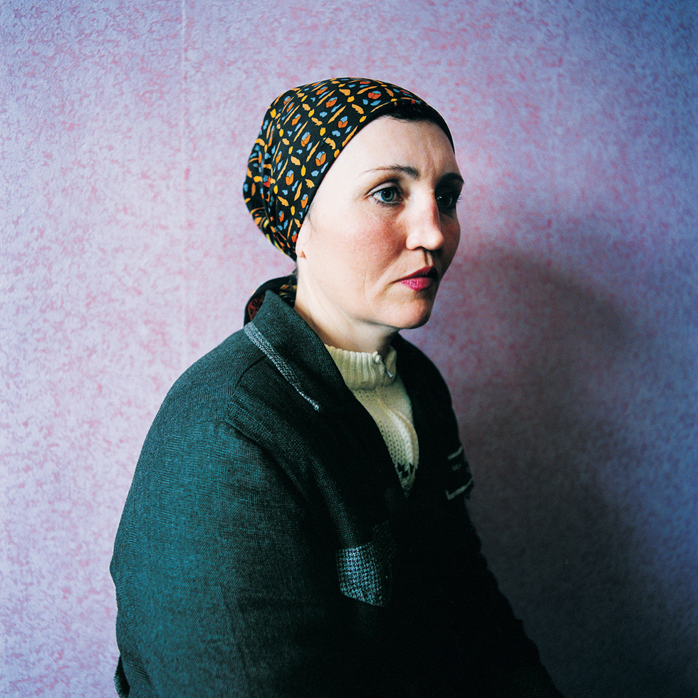 This is a photo of a woman in three-quarter profile with a head scarf and prison uniform in front of a purple wall.