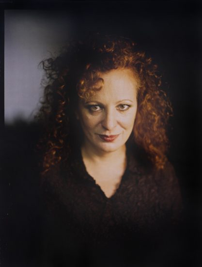 This is a color photographic portrait of a woman with red curly hair.