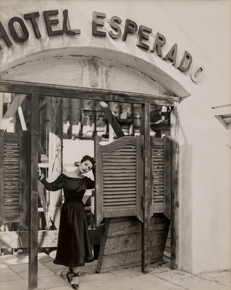 This is a black-and-white photograph of a woman in a black dress in front of the Hotel Esperado.