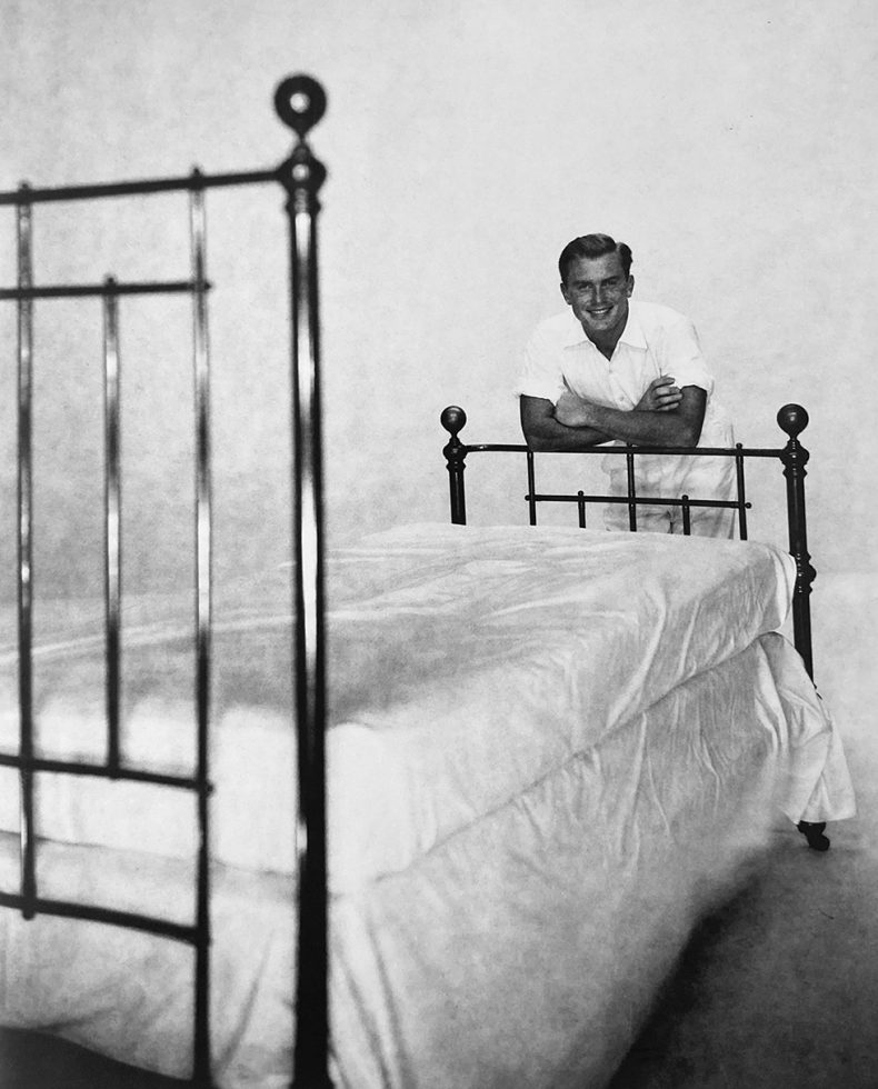 Alexander Jensen Yow leaning over an iron bedframe